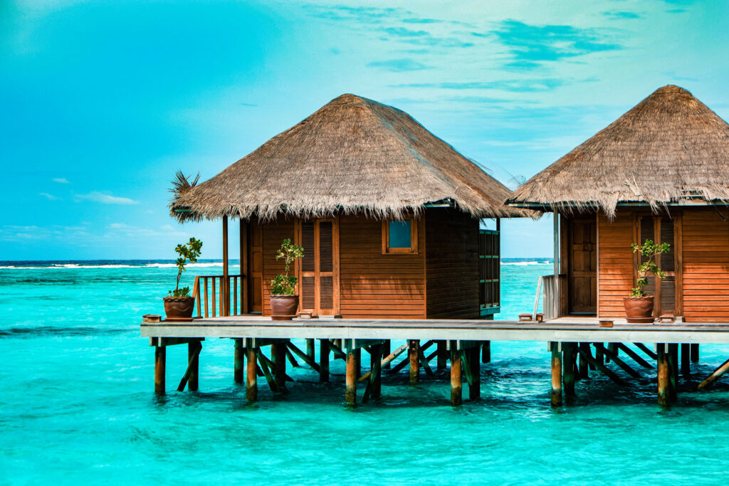 Overwater bungalows with thatched roofs connected by a wooden dock over turquoise water.