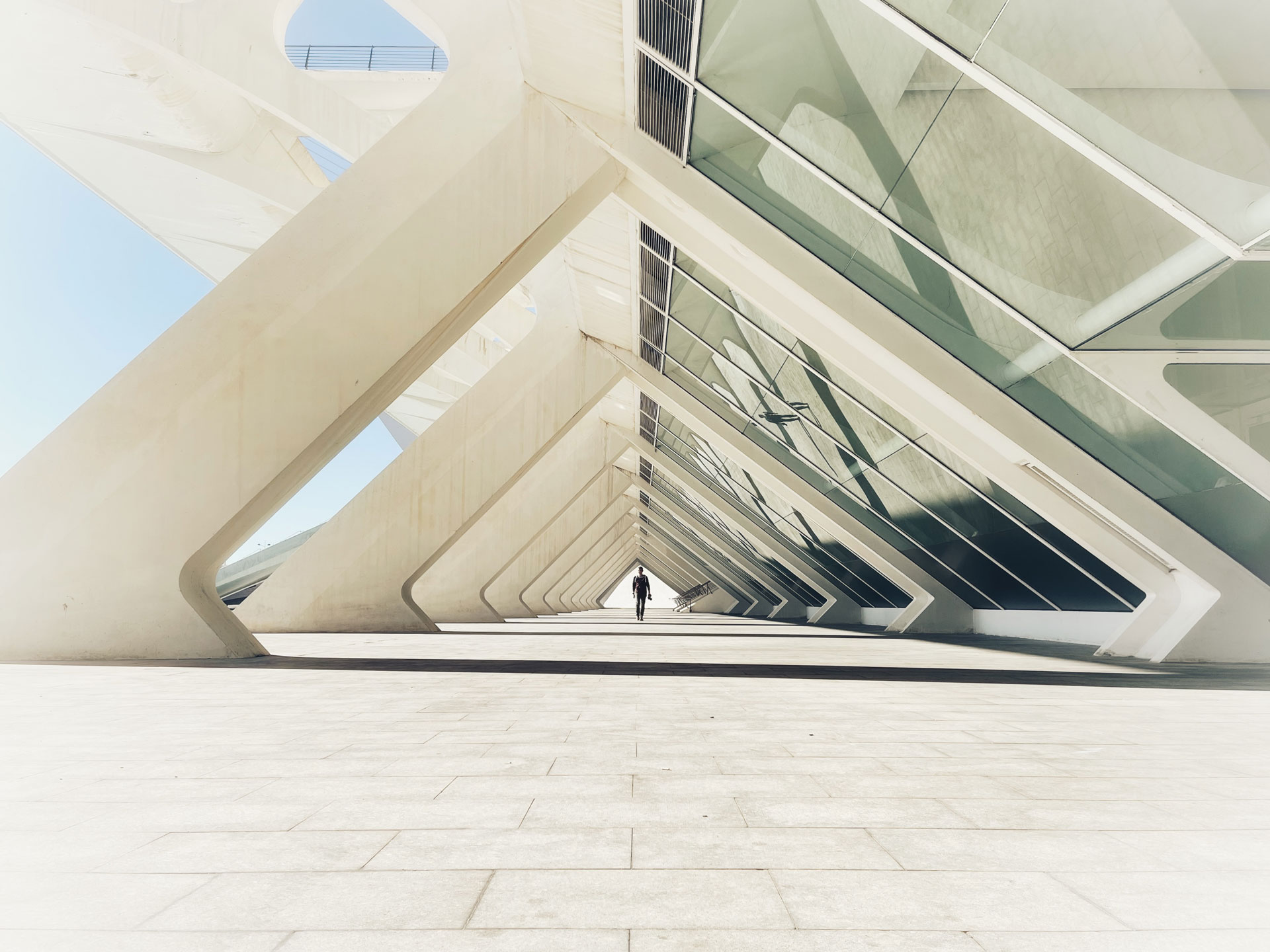 Person walking through a modern building's angular concrete and glass covered walkway.
